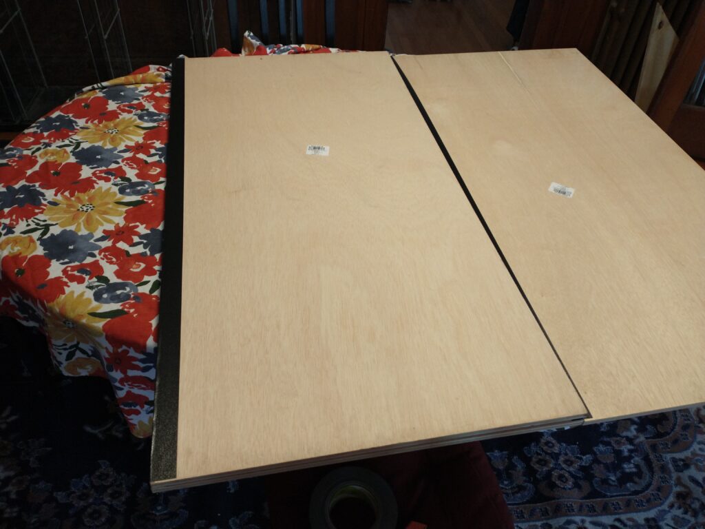 A third board lying on top of the second with a tape hinge in place.