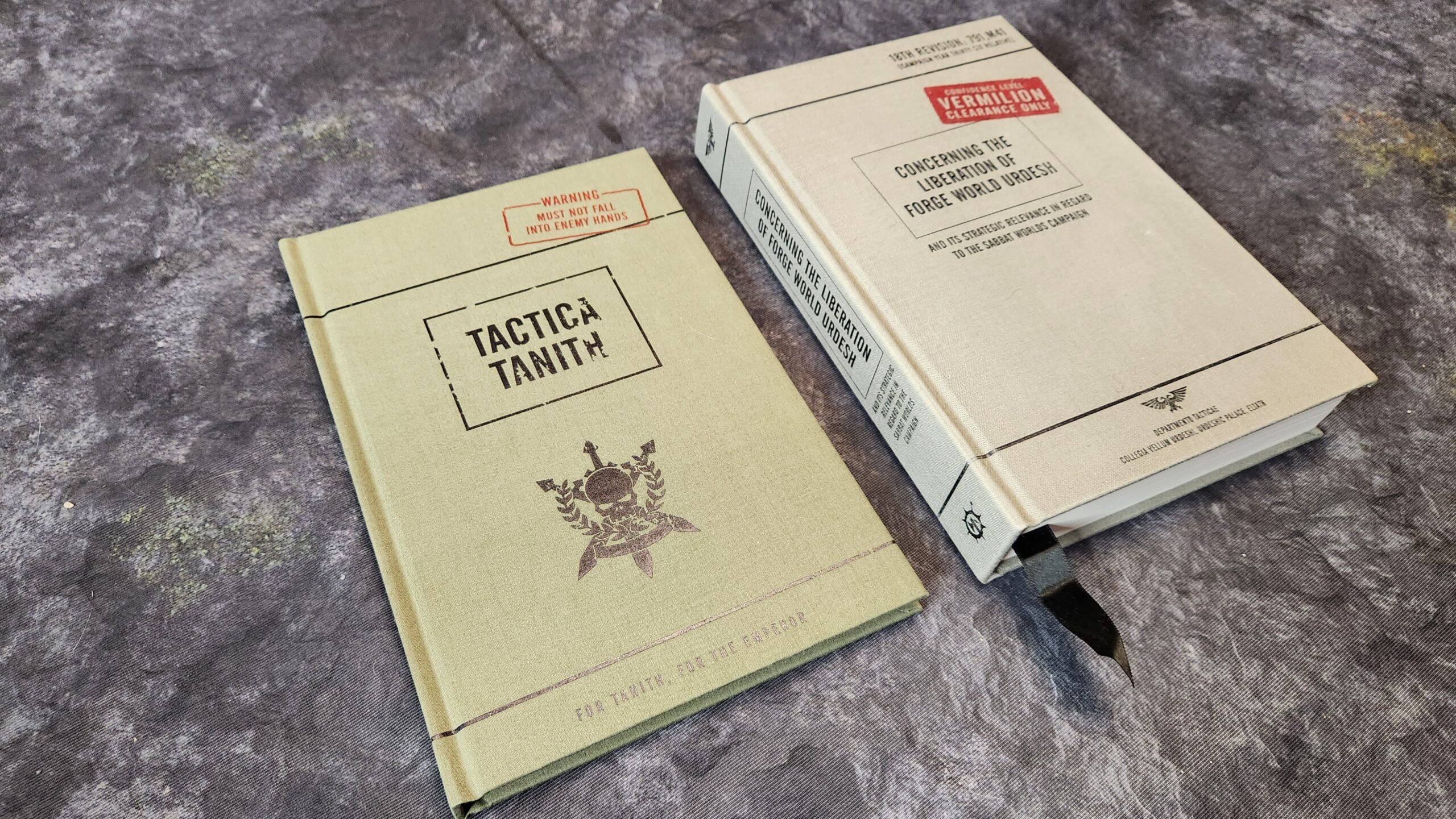 A picture showing two in-world Warhammer 40K books named Tactica Tanith and Concerning the Liberation of Forge World Urdesh.
